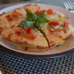 Sliced flatbread topped with melted cheese, diced vegetables, and fresh herbs served on a plate.