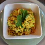 Bowl of turmeric-spiced scrambled eggs or vegetable dish garnished with fresh herbs.