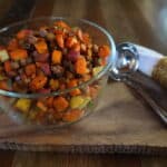 Glass bowl filled with roasted vegetables on a wooden table with a serving spoon nearby.