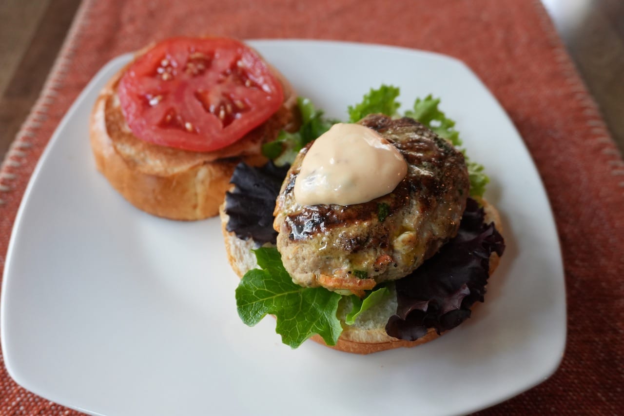 Open-faced burger with a vegetable patty, leafy greens, tomato slice, and sauce served on a plate.